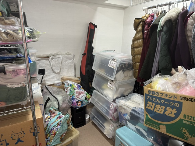 衣類を掛け、収納ケースや段ボールを置いたトランクハウス24江東千石の3.4帖の区画